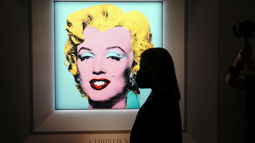 the silhouette of a woman looking at the print hanging on a wall. The print is of Marilyn Monroe's face, highlighted in blue