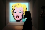 the silhouette of a woman looking at the print hanging on a wall. The print is of Marilyn Monroe's face, highlighted in blue