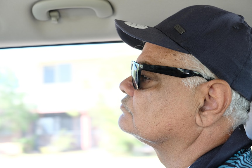 A man with sunnies and a hat sitting in a car.