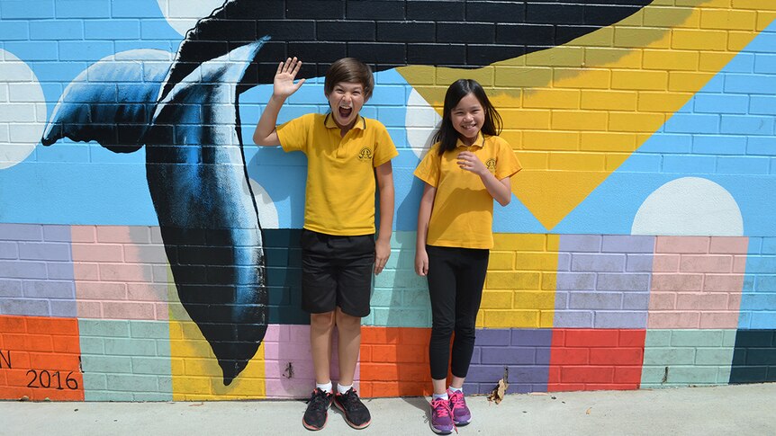 Colour photo of primary school students Lawson and Dao Anh posing in front of brightly coloured mural wall.