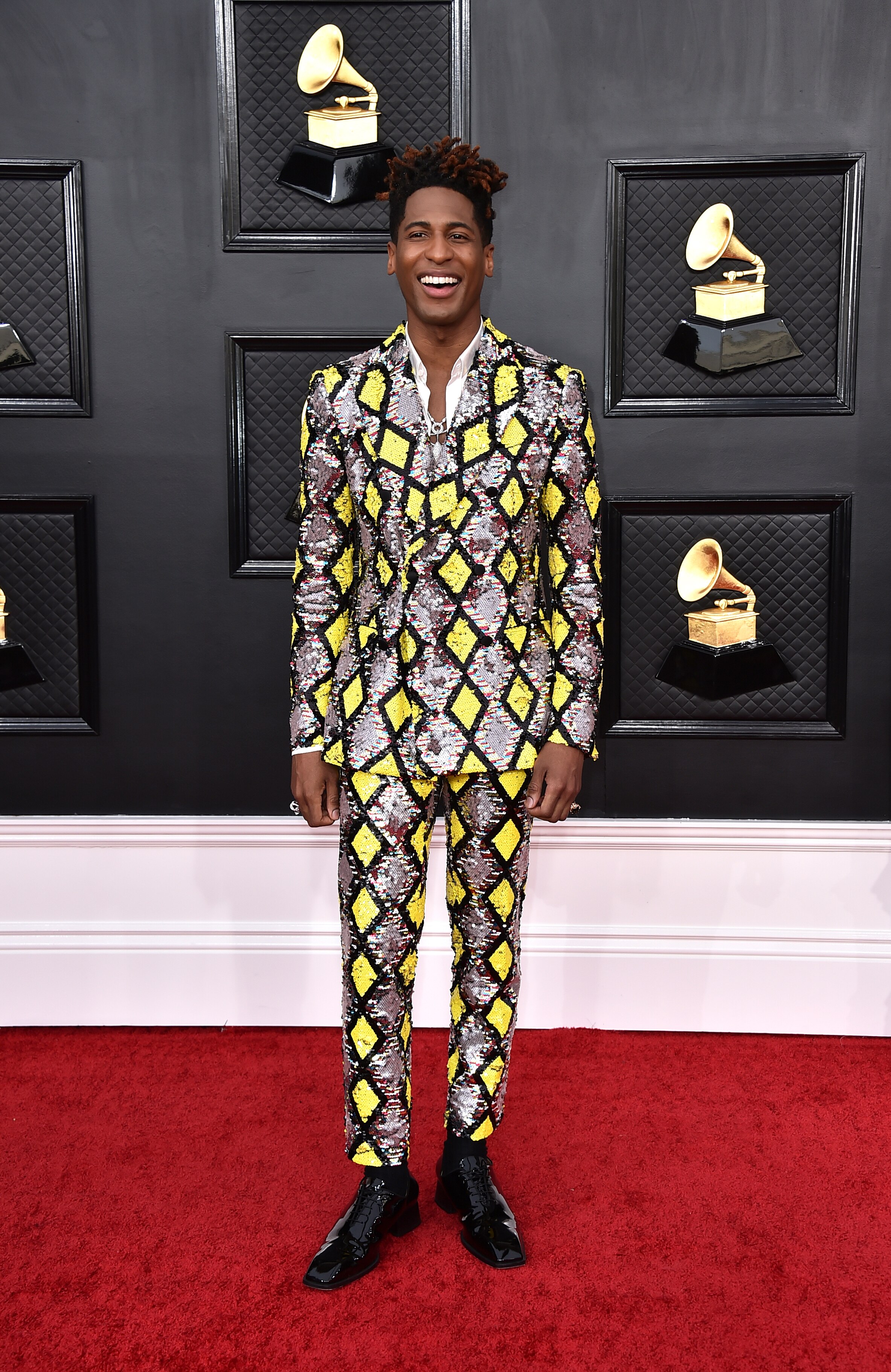 singer jon batiste smiles on the grammys red carpet wearing a fully sequinned suit with a silver, black and neon green pattern