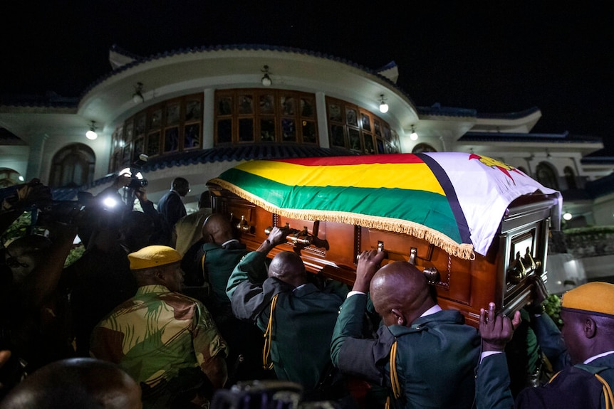 Robert Mugabe's coffin, draped in the Zimbabwean national flag, is carried by soldiers as it arrives at his official residence.