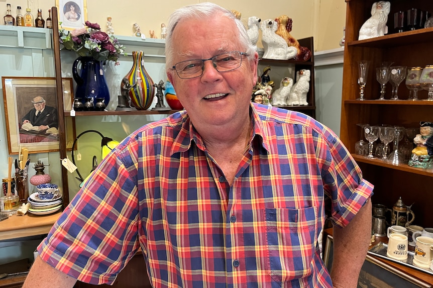 A smiling older man stands in an antique store.
