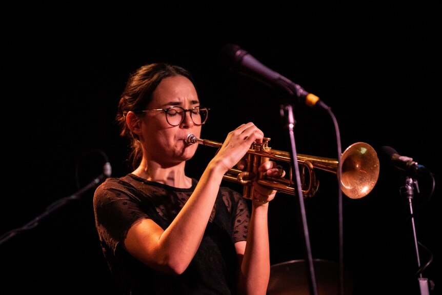 Jessica Carlton plays trumpet on stage. There is a microphone in the picture.