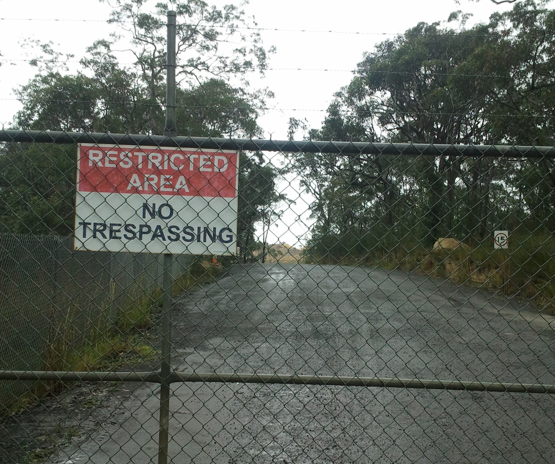 Large locked gated entrance to the Mangrove Mountain dump with a 'no trespassing' sign.
