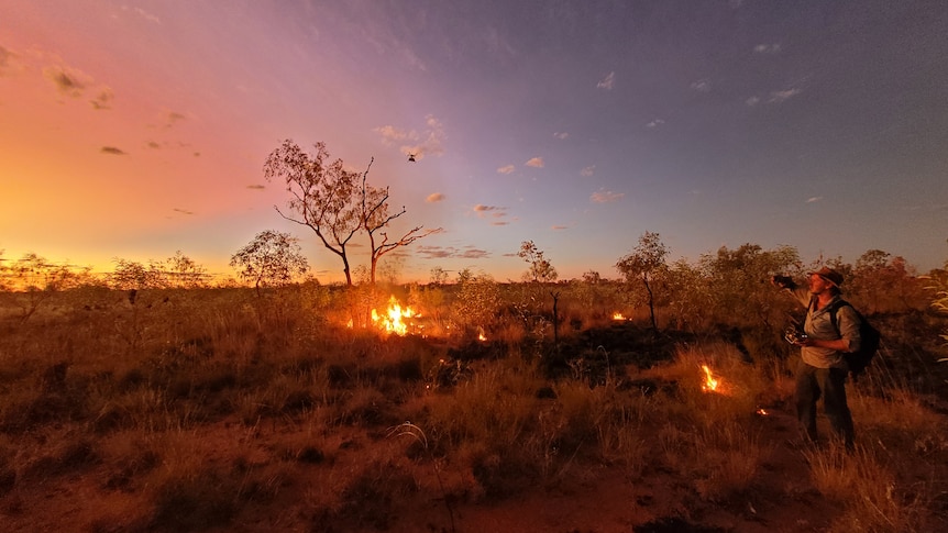 A man flies a drone over a bushfire.