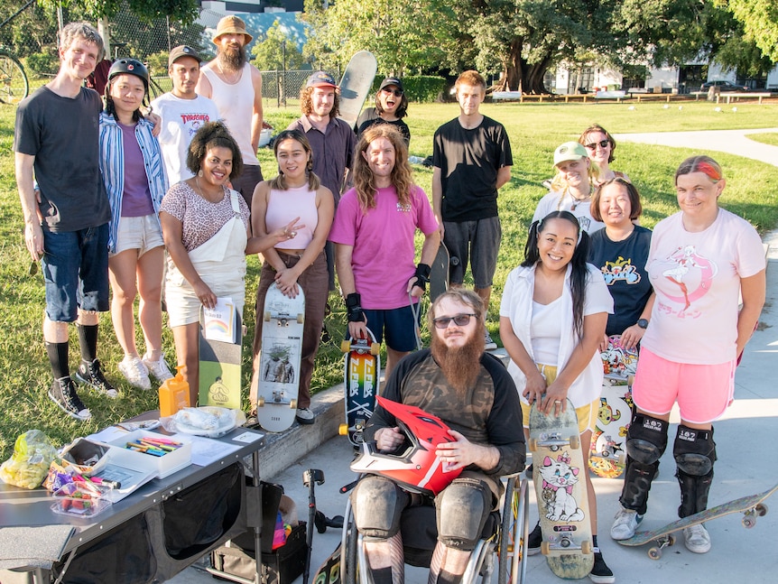 A group photo of 15 people, some holding skateboards, all smiling at the camera.