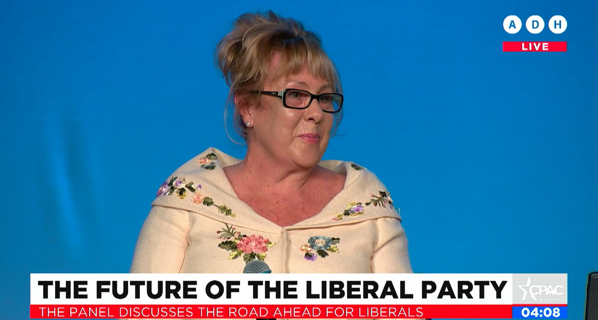 McQueen smiles holding a microphone while on stage, a TV strap reads 'The Future of the Liberal Party