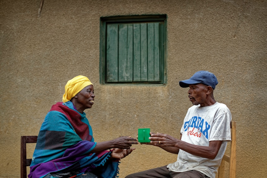 Genocide survivor Laurencia Mukalemera, left, a Tutsi, is offered a cup of water by Tasian Nkundiye, a Hutu