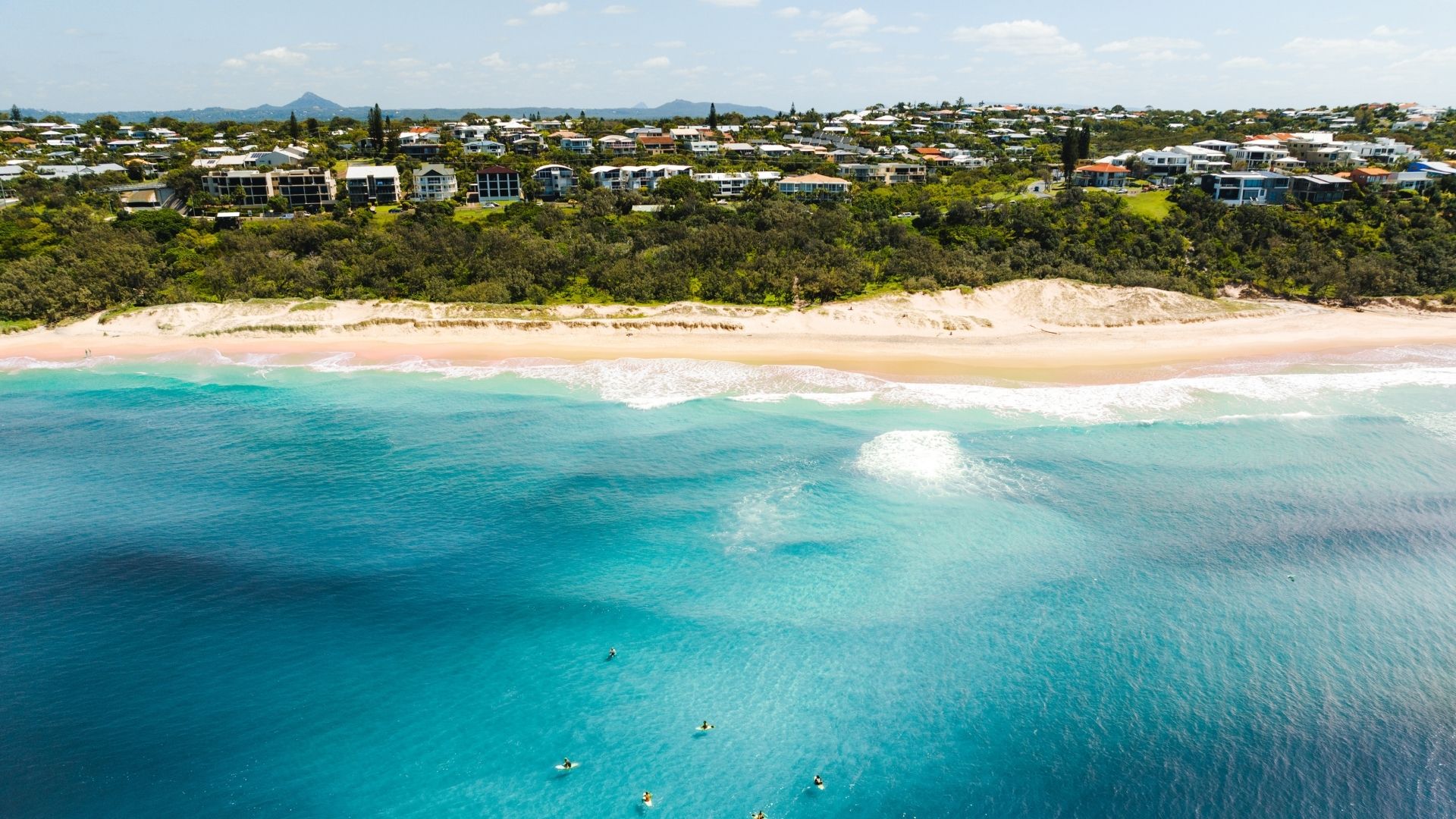 Una vista aérea de una playa con hileras de casas detrás.