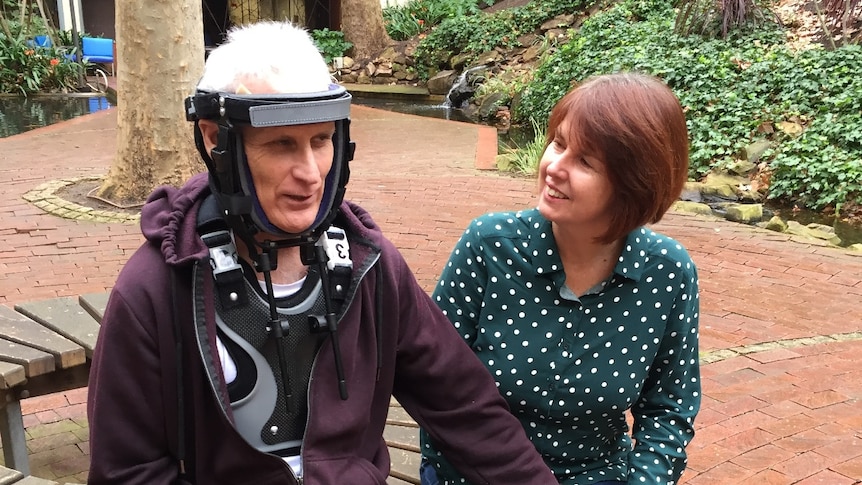 A man in a neck brace holds hand with a woman.