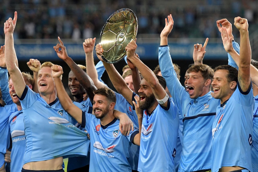 Sydney FC's 2016/17 team raise the shield and their arms in celebration.
