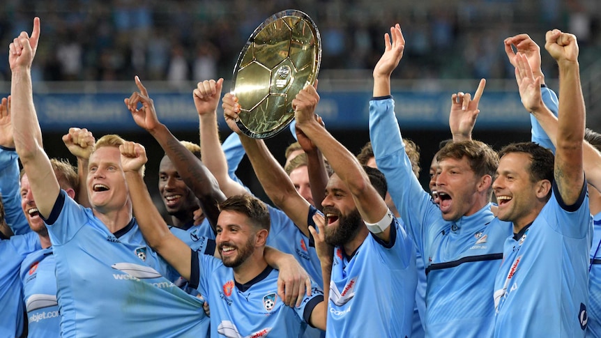 Sydney FC's 2016/17 team raise the shield and their arms in celebration.
