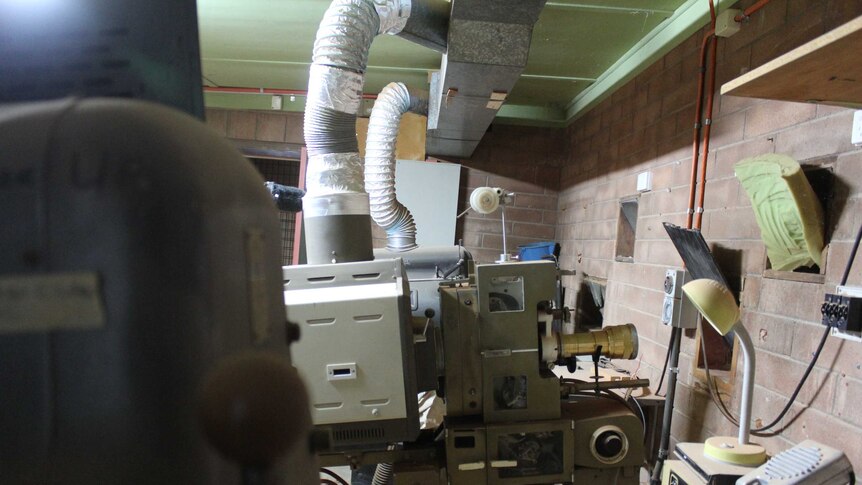 Old projection units sit covered in light red dust in a disused brick building