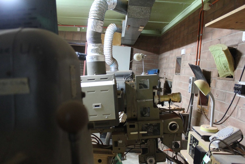 Old projection units sit covered in light red dust in a disused brick building