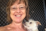 A woman smiles while holding a small dog