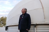 A man in dark clothing stands next to a white observatory.