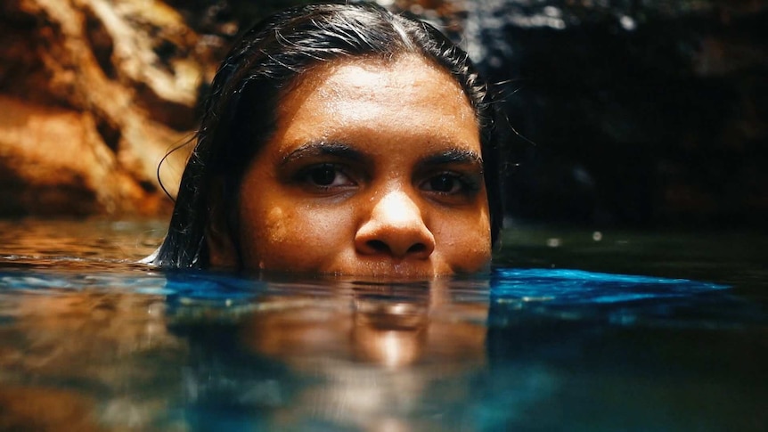 A woman face half submerged in a waterhole.