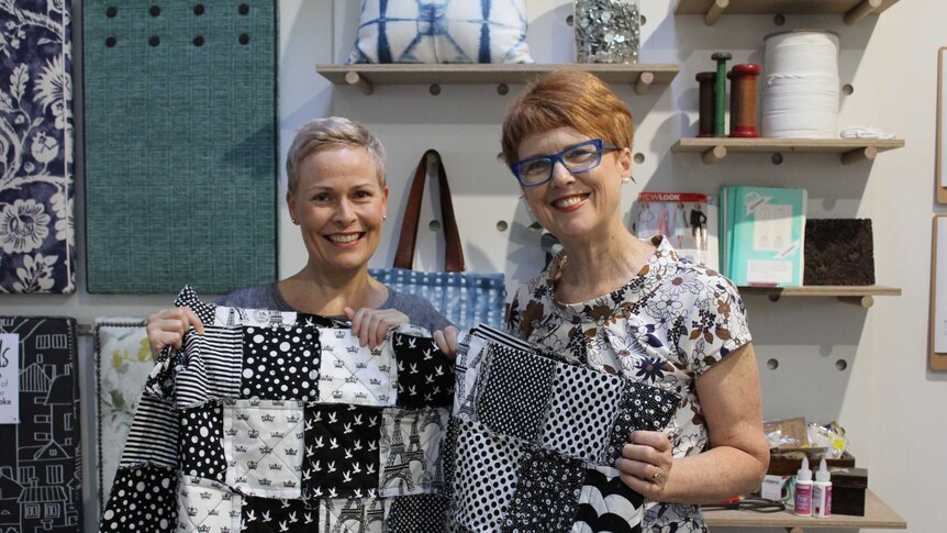 Jenni Langan and Julie Hillier inside the Ministry of Hand Made sewing workshop holding a black and white quilt.