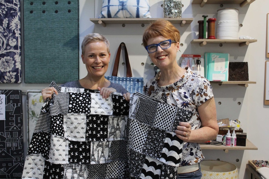 Jenni Langan and Julie Hillier inside the Ministry of Hand Made sewing workshop holding a black and white quilt.
