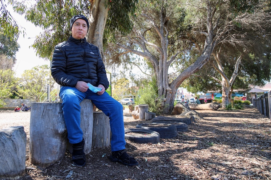 A man wearing a black jacket and blue jeans in a park.