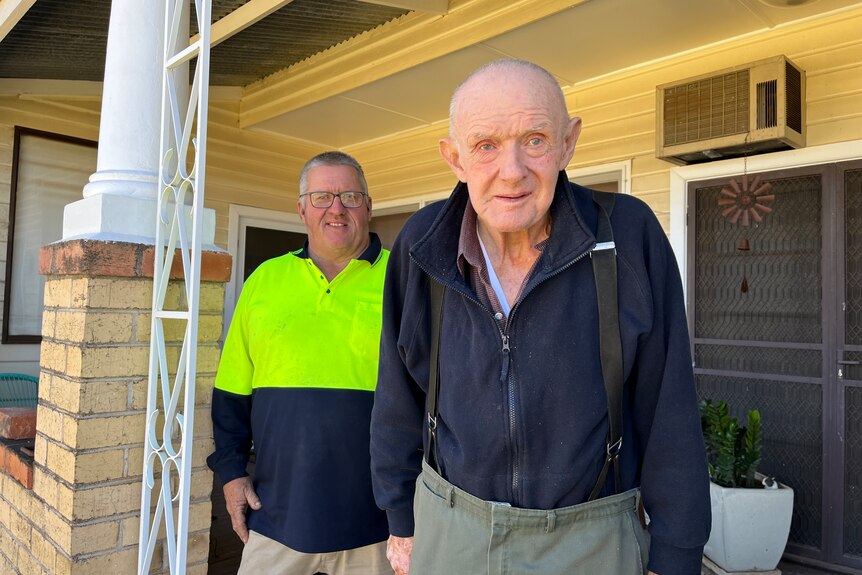 Two men stand on the porch of a house looking at the camera