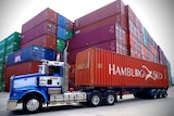 A truck carries a Hamburg Sud shipping container in front of a stack of other containers at Sydney's Port Botany.