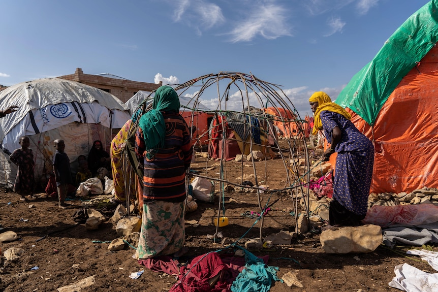 Women in brightly coloured clothes build a shack out of sticks and scraps of fabric