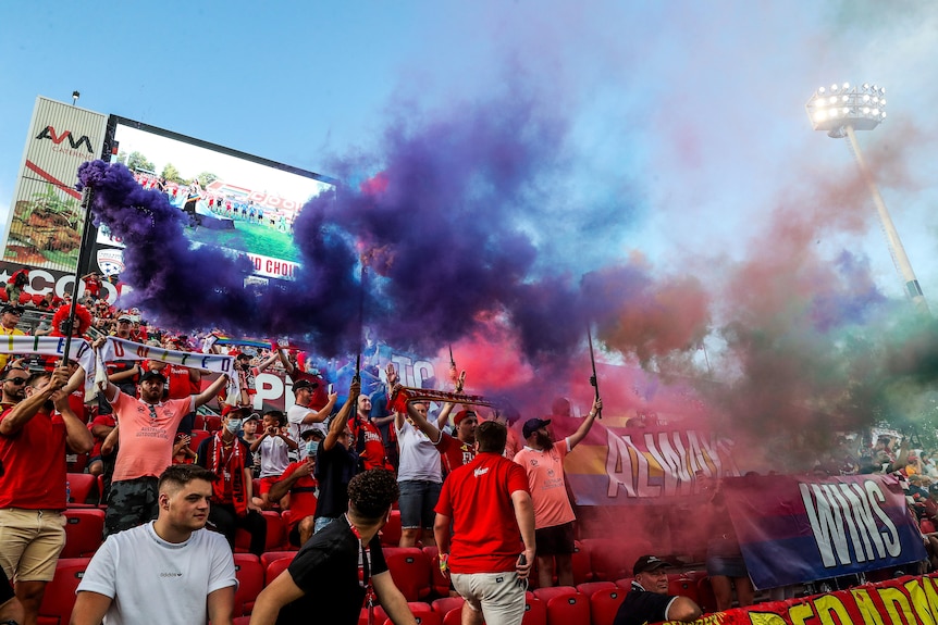 Soccer fans hold up signs and smoke flares during a match