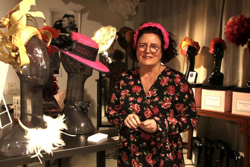 Wendy stands smiling in her store, surrounded by hats she has designed.