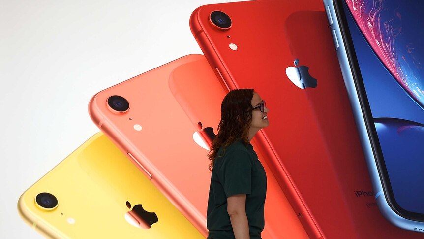 A woman walks past a backdrop showing four different-coloured iPhones splayed out on top of each other