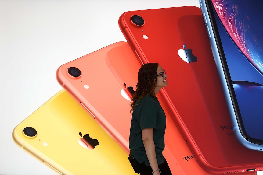 A woman walks past a backdrop showing four different-coloured iPhones splayed out on top of each other