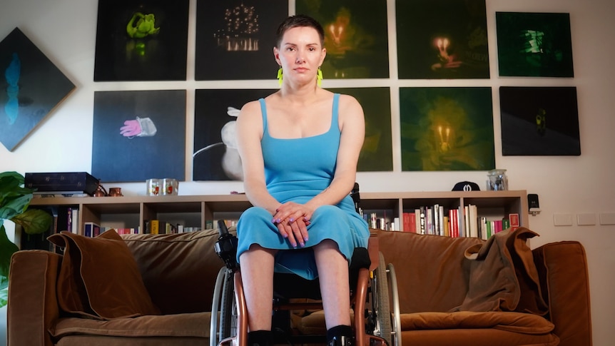 A woman in a blue dress sitting in a wheelchair in her home.