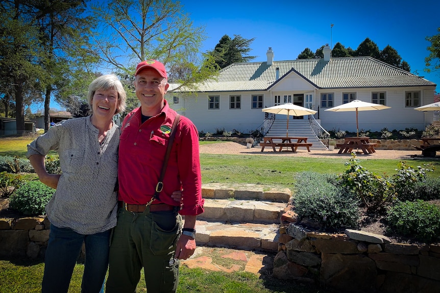 Man and woman smiling in foreground with restaurant building in background.