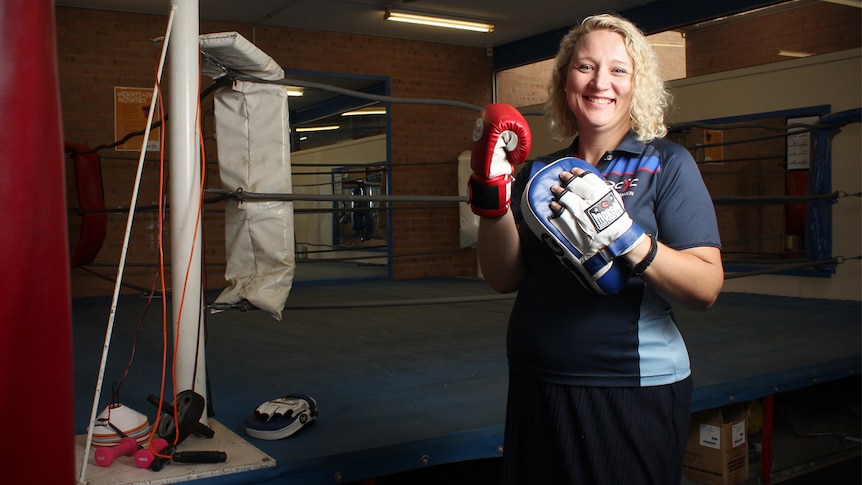 Sam Kettlewell stands in the PCYC Shoalhaven boxing gym wearing a glove and focus mit.