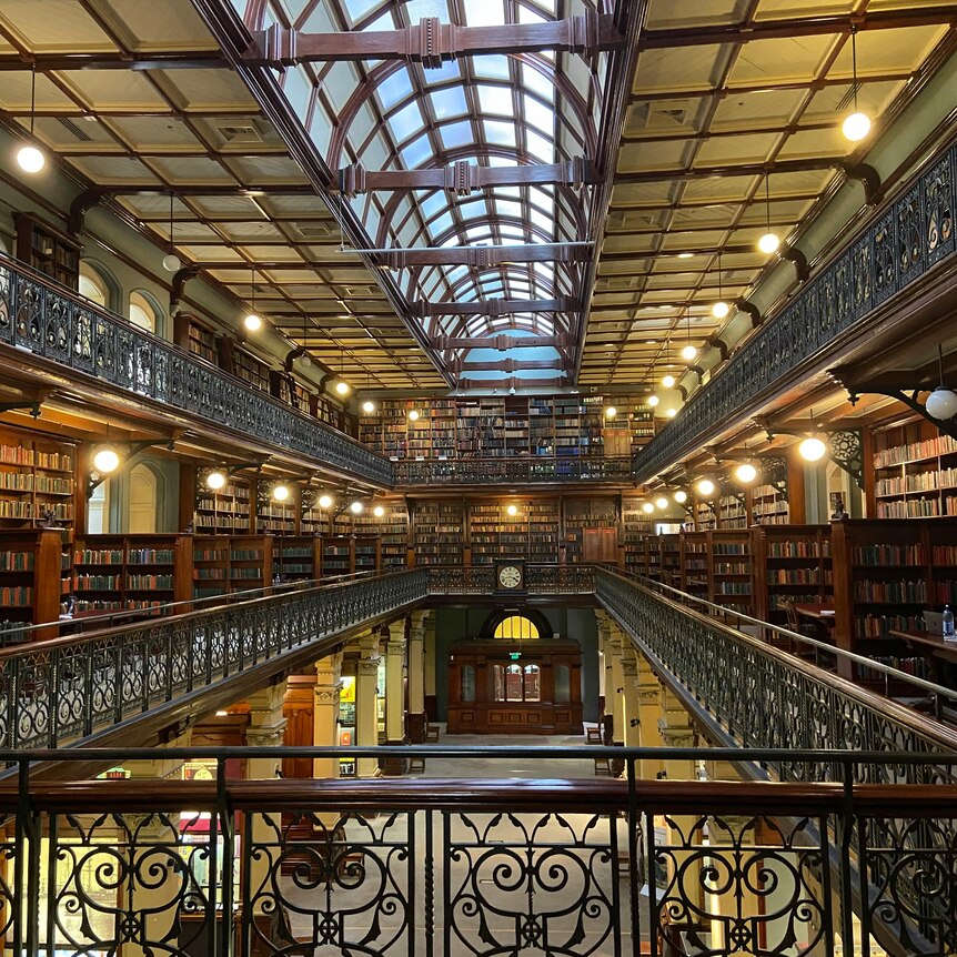 Glass-roofed building with rows of bookshelves around the edge of the building taken from a landing