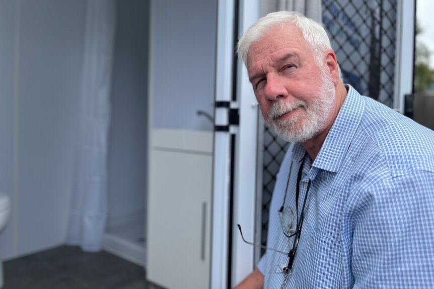 Man in a blue collared shirt with a white beard stares at the camera.