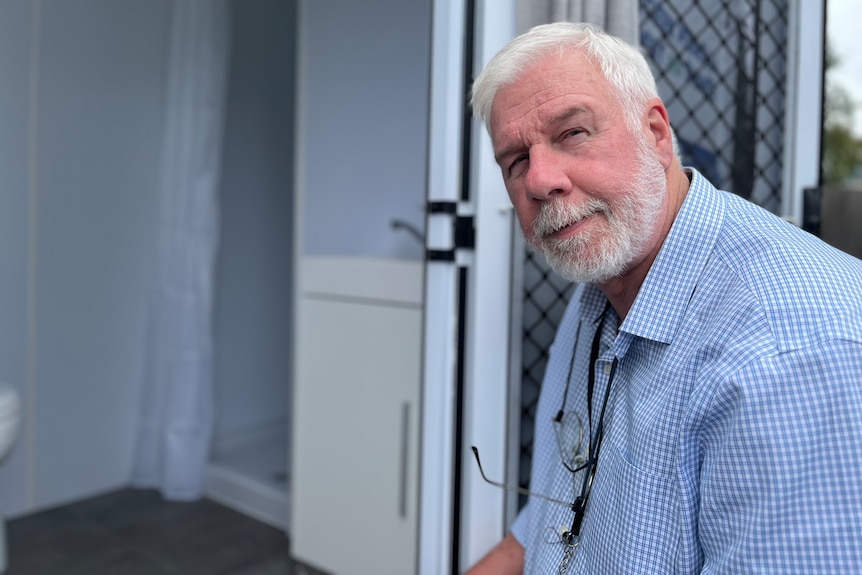 Man in a blue collared shirt with a white beard stares at the camera.