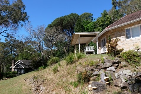 A picture of a cottage on a hill with rocks in front of it and another cottage in the far background.