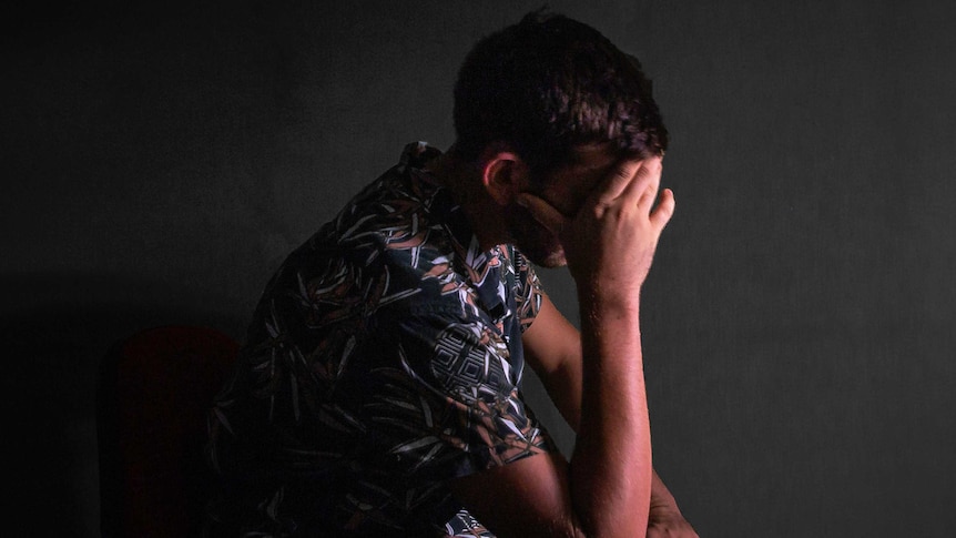 A man sits holding his head in his hands.