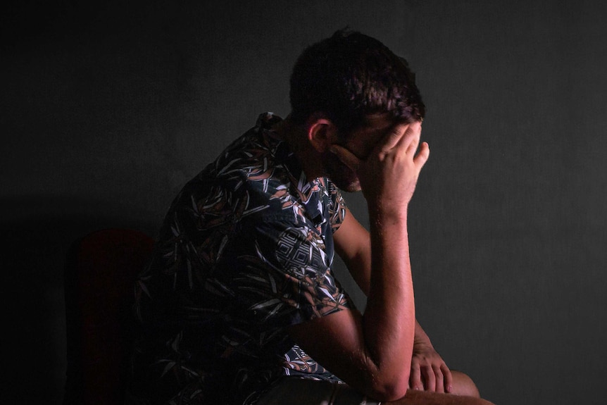 A man sits holding his head in his hands.