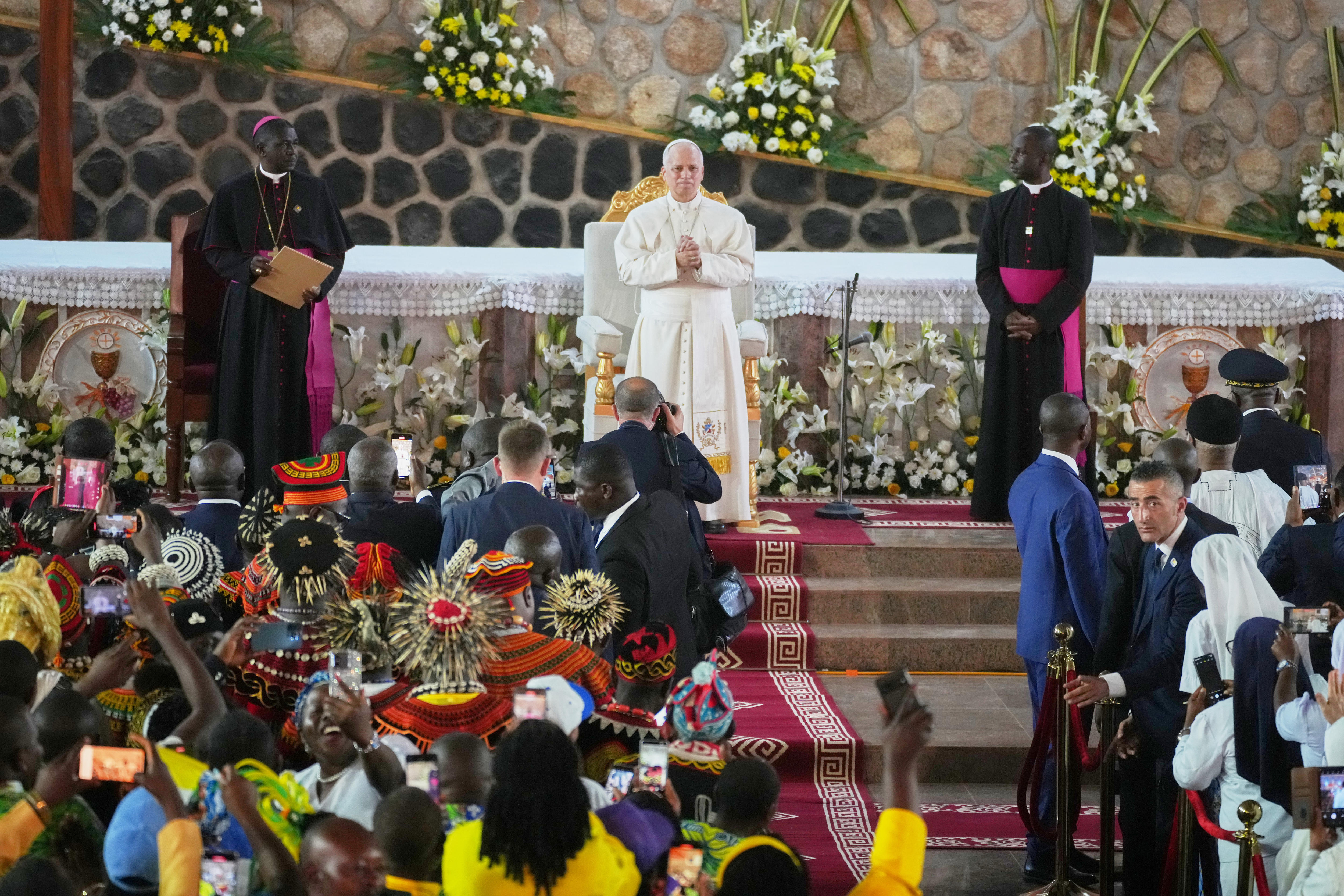 A man in white robes stands on an altar addressing a crowd.