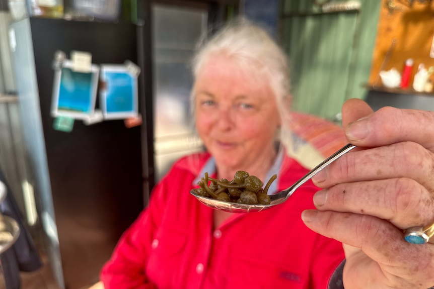 Liz holds out a spoon filled with preserved capers. 