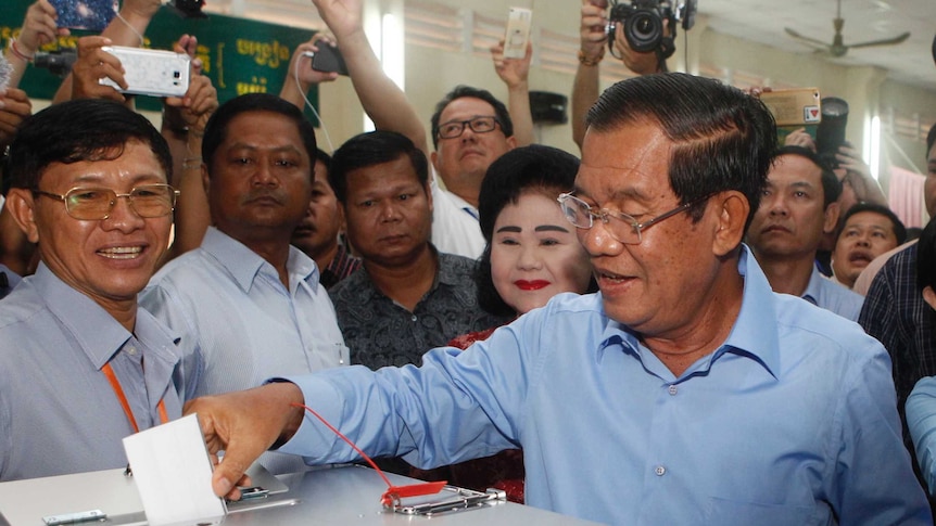 Hun Sen places his voting slip in the ballot box surrounded by people.