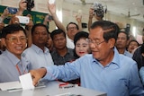 Hun Sen places his voting slip in the ballot box surrounded by people.