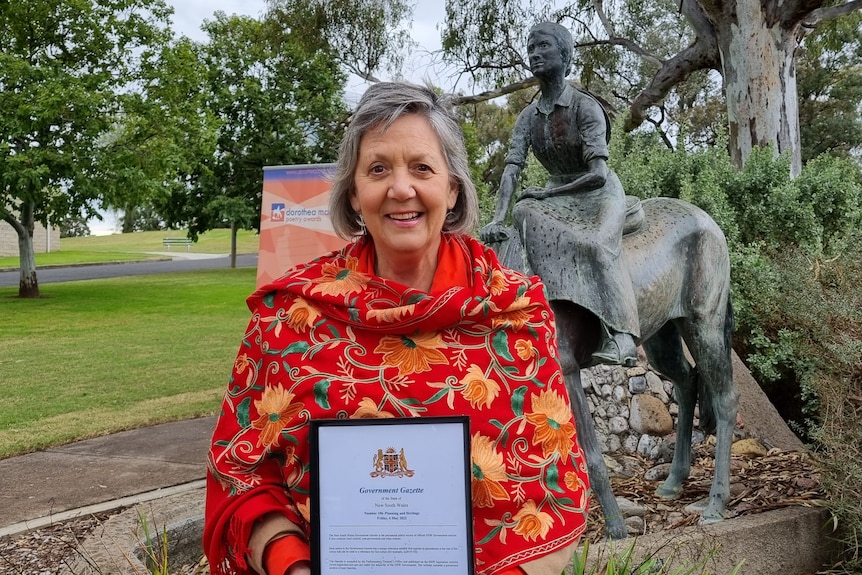 A woman standing in front of a statue of a horse with a framed certificate.