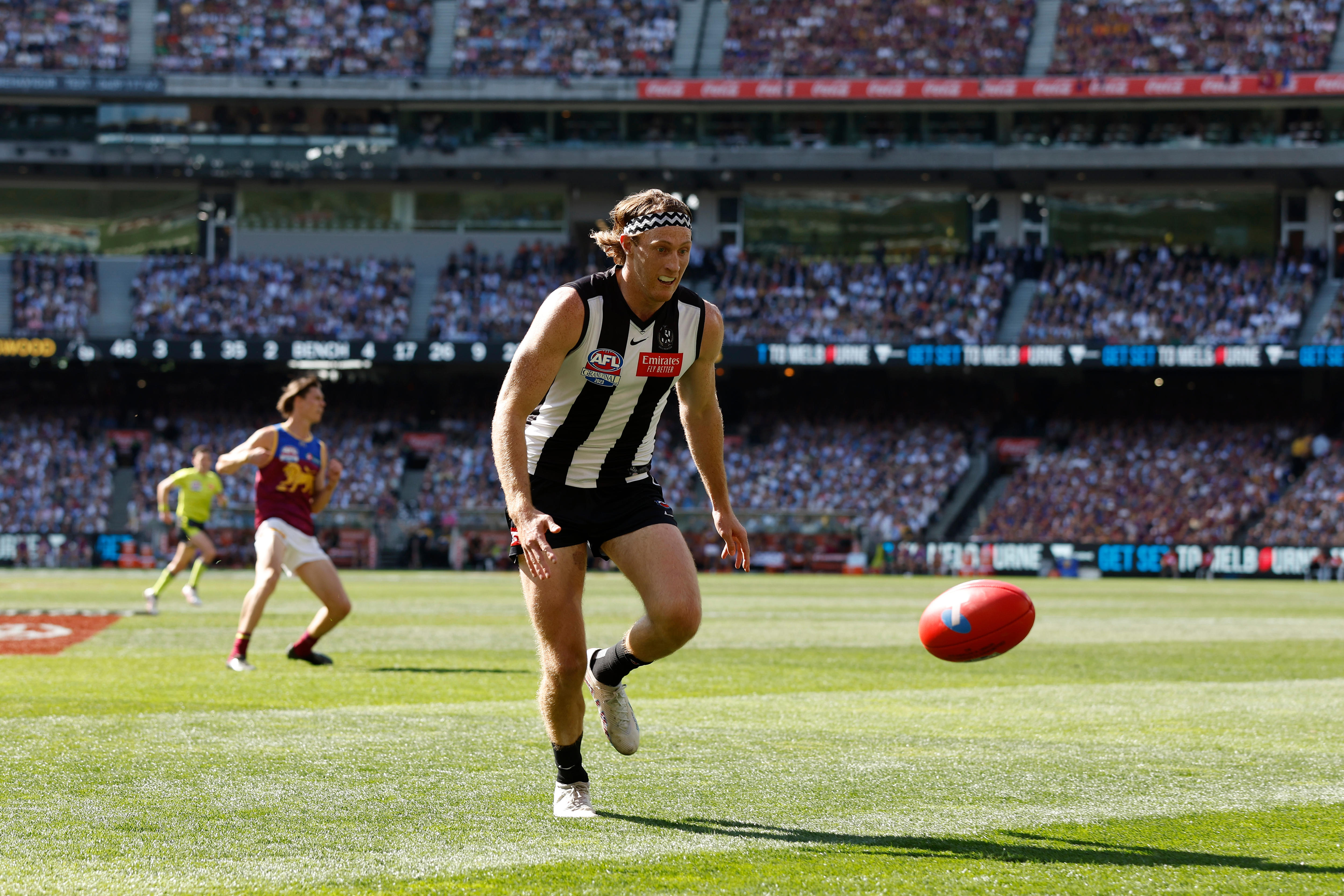 A Collingwood AFL player wearing a headband has eyes on the ball bouncing in front of him at the MCG in a grand final.