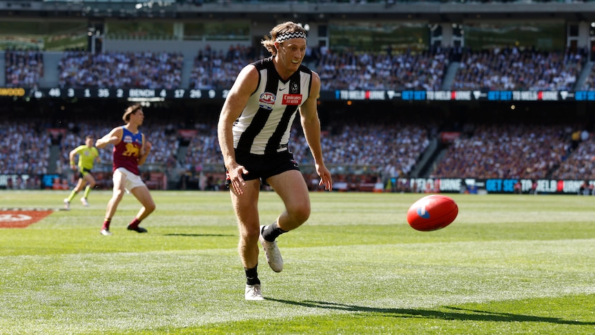 A Collingwood AFL player wearing a headband has eyes on the ball bouncing in front of him at the MCG in a grand final.