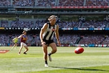 A Collingwood AFL player wearing a headband has eyes on the ball bouncing in front of him at the MCG in a grand final.
