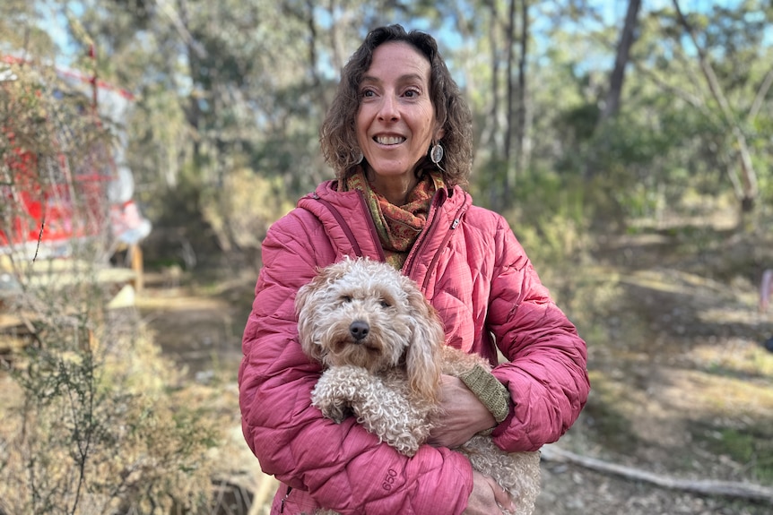 A woman in a pink puffer jacket standing with her dog.